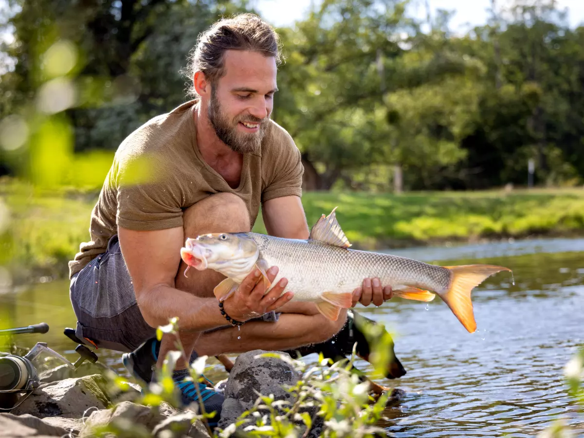 Angler mit Ausrüstung und gefangener Barbe am Fluss