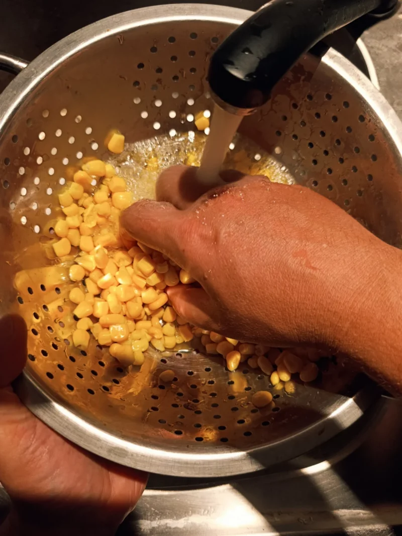 Dosenmais wird über einem Sieb ausgewaschen, um ihn länger haltbar zu machen