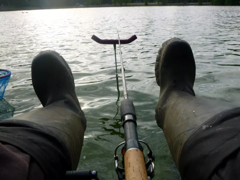 Angler mit Gummistiefeln und eine abgelegte Feederrute
