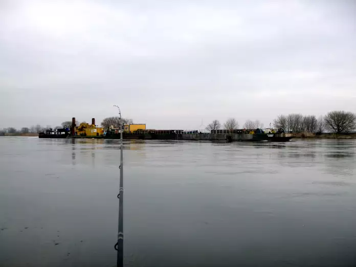 Angler mit Feederrute an der Elbe während ein Schiff fährt