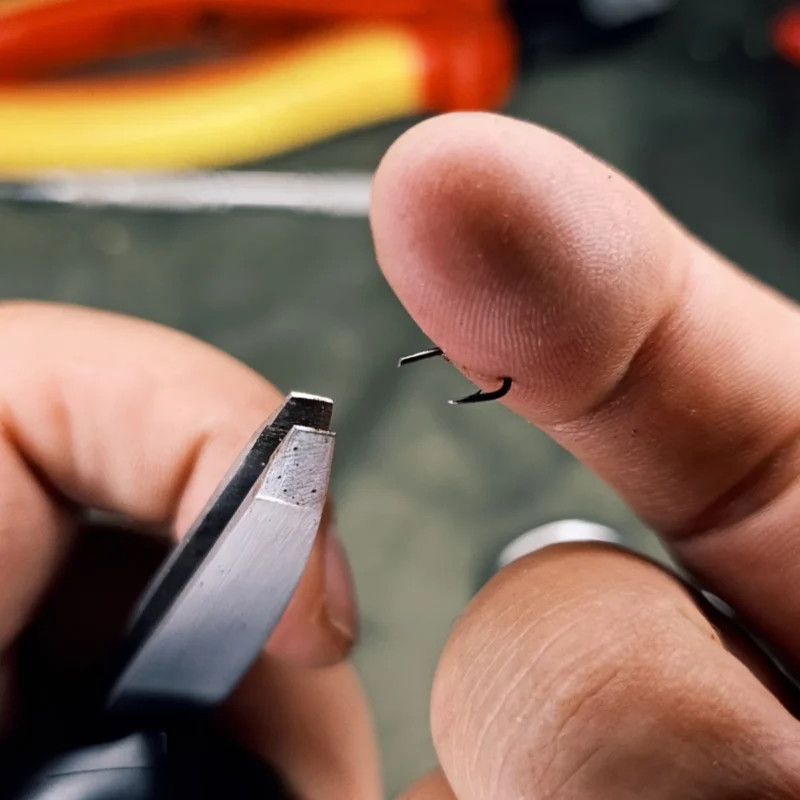 Haken mit der Pinzette greifen und durch den Finger bis zum Widerhaken bugsieren