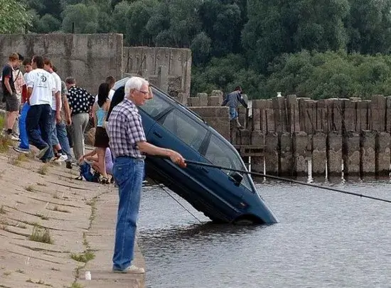 lustiges Angelbild: Auto rollt ins Wasser, Angler macht in ruhe weiter