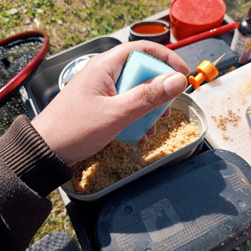 Method Feeder Futter wird mit Wasser aus einem Schwamm befeuchtet